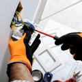 Technician wiring an electrical panel with a screwdriver and gloves
