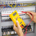 Technician testing an electrical control panel with a yellow multimeter and red probe leads