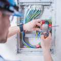 Electrician wiring a circuit breaker panel with colorful wires and a multimeter