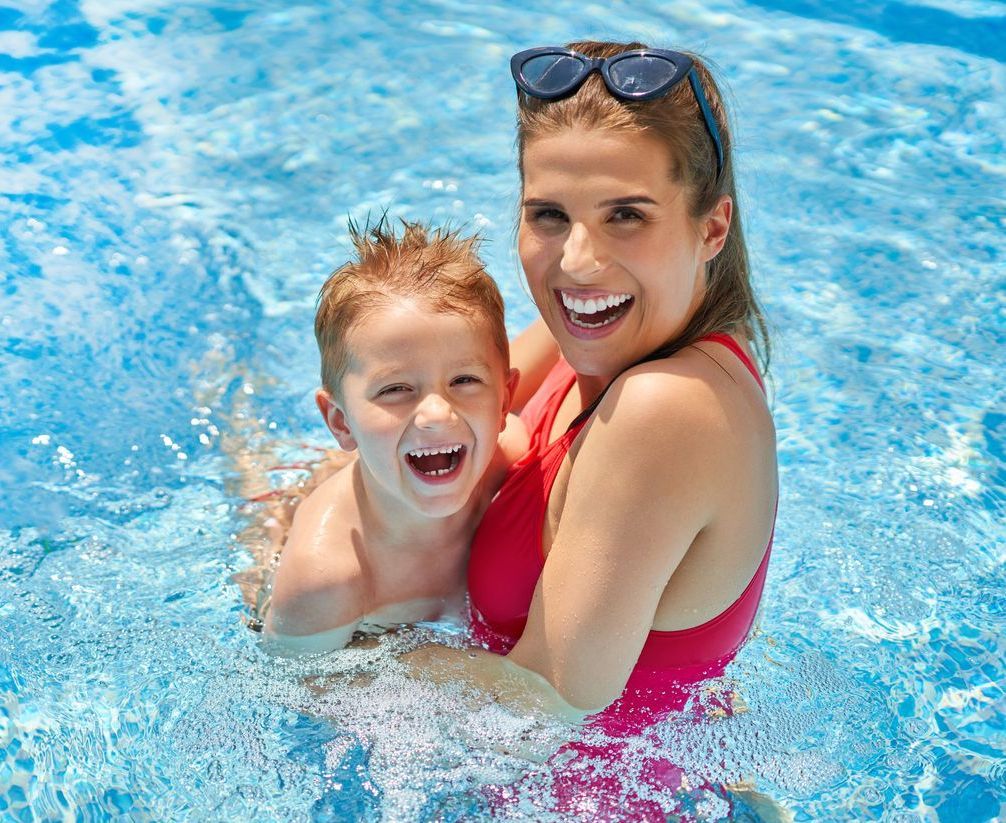 Cute boy with his mother playing in swimming pool during summer