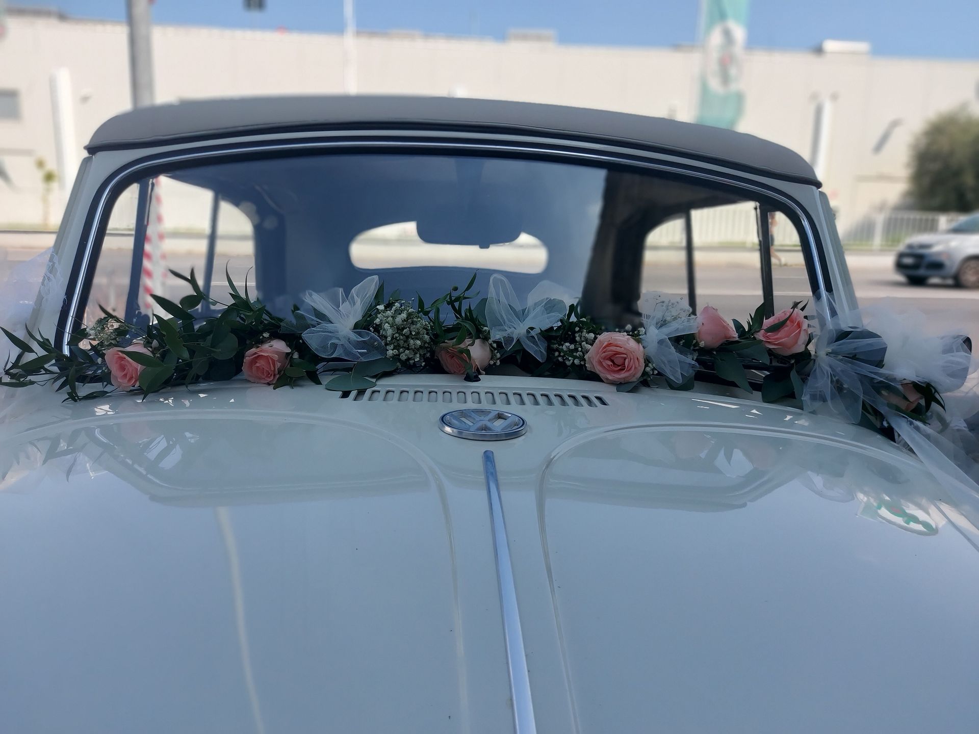 Un'auto bianca con dei fiori sul parabrezza è parcheggiata davanti a un edificio.
