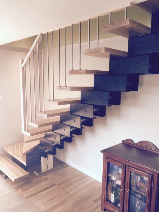 Escalier flottant moderne avec supports en métal foncé et marches en bois clair, placé à côté d'une armoire en bois.