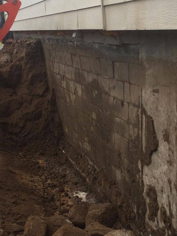 Gros plan sur un mur de fondation excavé, constitué de blocs de béton et partiellement recouvert de terre humide.