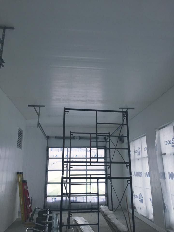Vue intérieure d'une pièce en construction avec des murs blancs, un plafond fini, des échafaudages métalliques et des fenêtres.