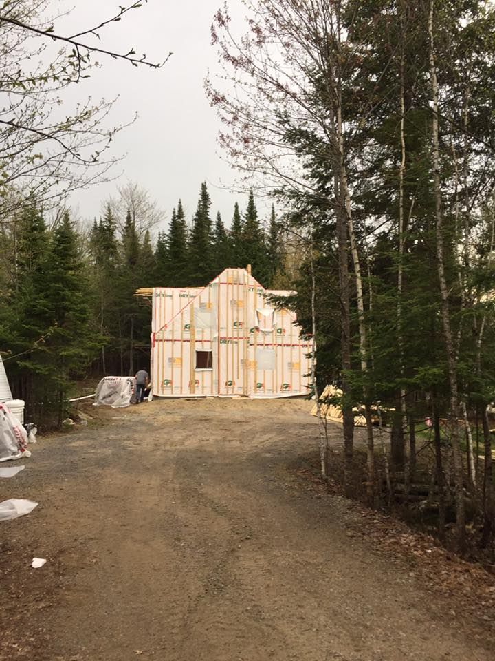 Une structure en bois partiellement construite se dresse dans une clairière entourée d'une dense forêt de conifères.