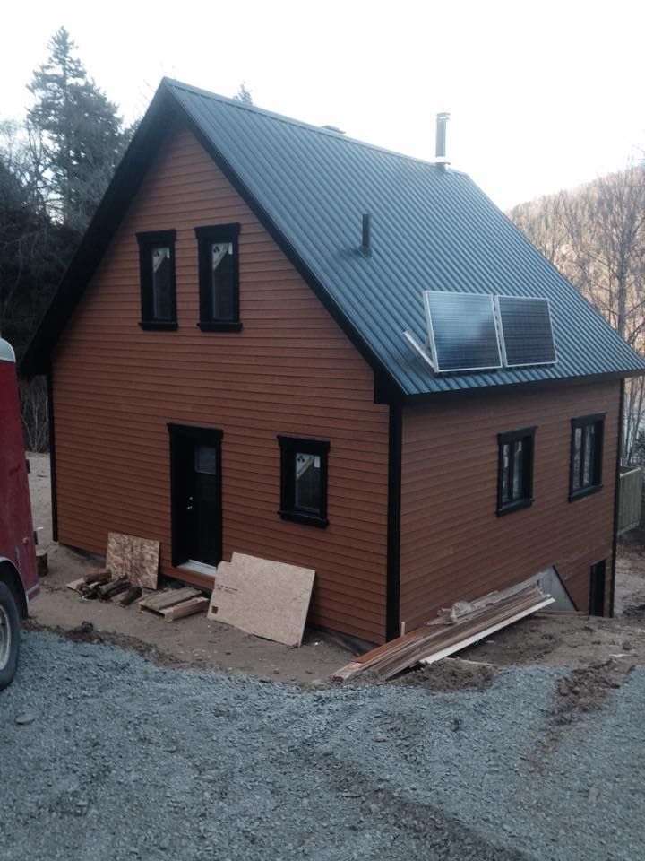 Maison à deux étages en construction, avec un bardage horizontal brun, un toit en métal foncé et des fenêtres à cadre noir.