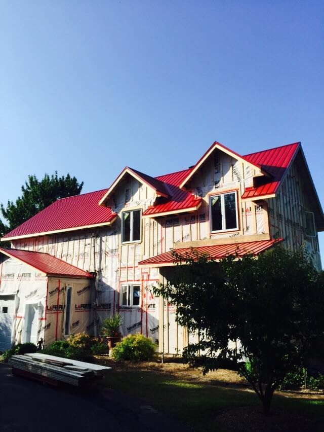 Une maison à deux étages en construction, avec un toit en métal rouge vif et une charpente apparente.