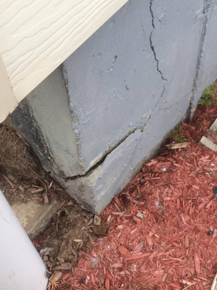 Gros plan sur un coin de fondation en béton présentant de larges et profondes fissures, situé à côté de paillis et de bardage.