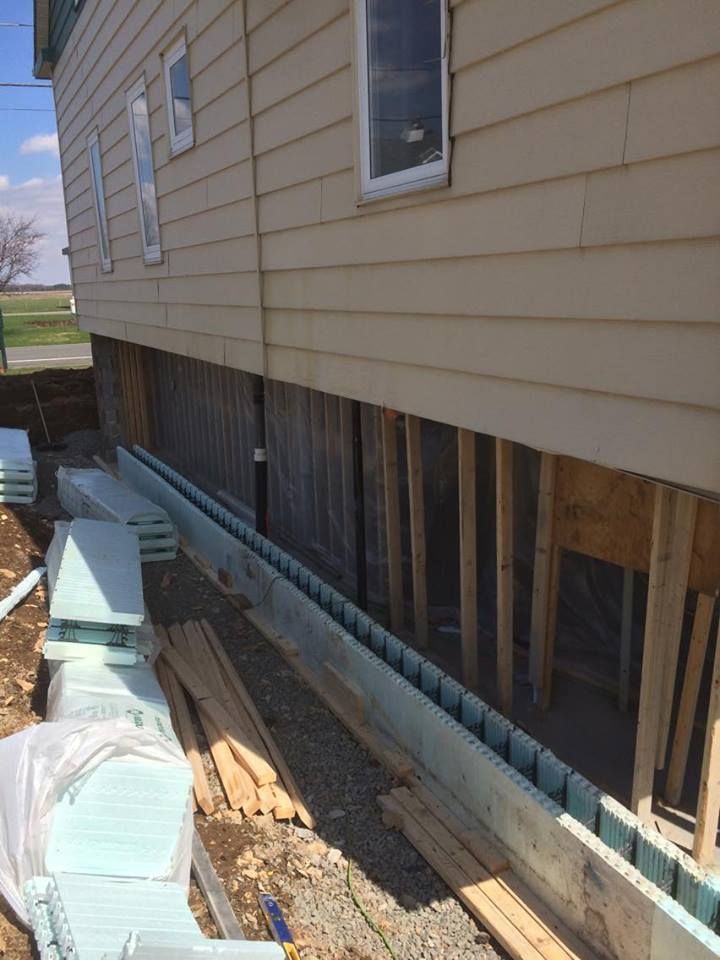 Vue extérieure d'une maison beige avec des montants muraux apparents et des panneaux d'isolation en mousse le long des fondations.