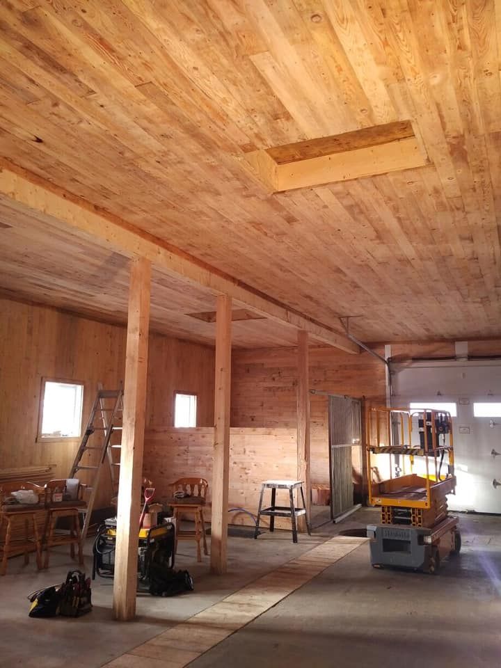 Vue intérieure d'un atelier en bois en construction, avec des poutres de soutien en bois, du matériel de travail et une échelle de plancher.