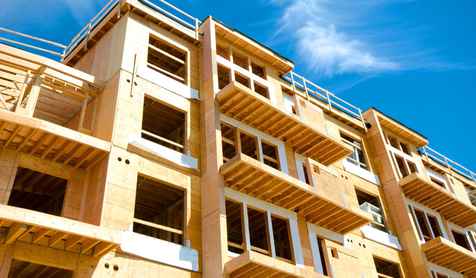 Immeuble d'appartements de plusieurs étages en construction, baigné de soleil, se détachant sur un ciel bleu.