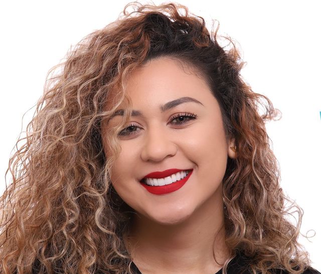 A woman with curly hair is smiling and wearing red lipstick