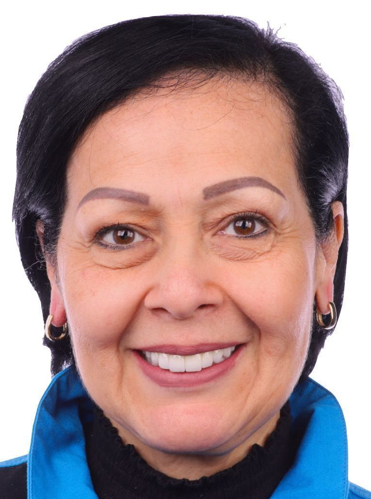 A woman wearing a blue jacket and earrings smiles for the camera