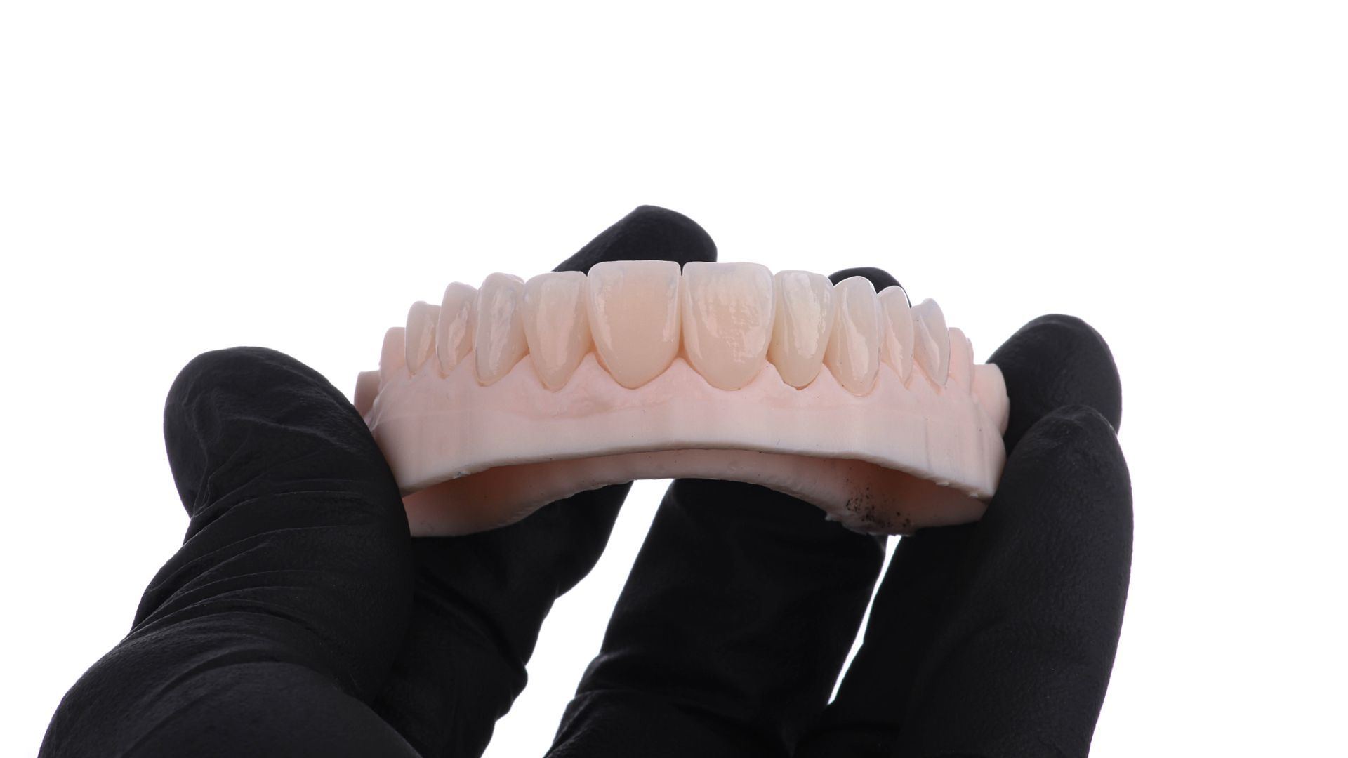 A person wearing black gloves is holding a model of teeth.