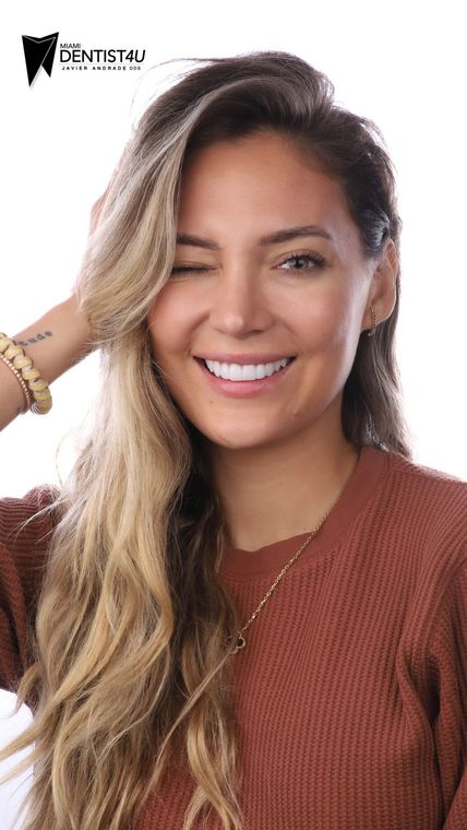A woman in a brown sweater is smiling and winking at the camera.