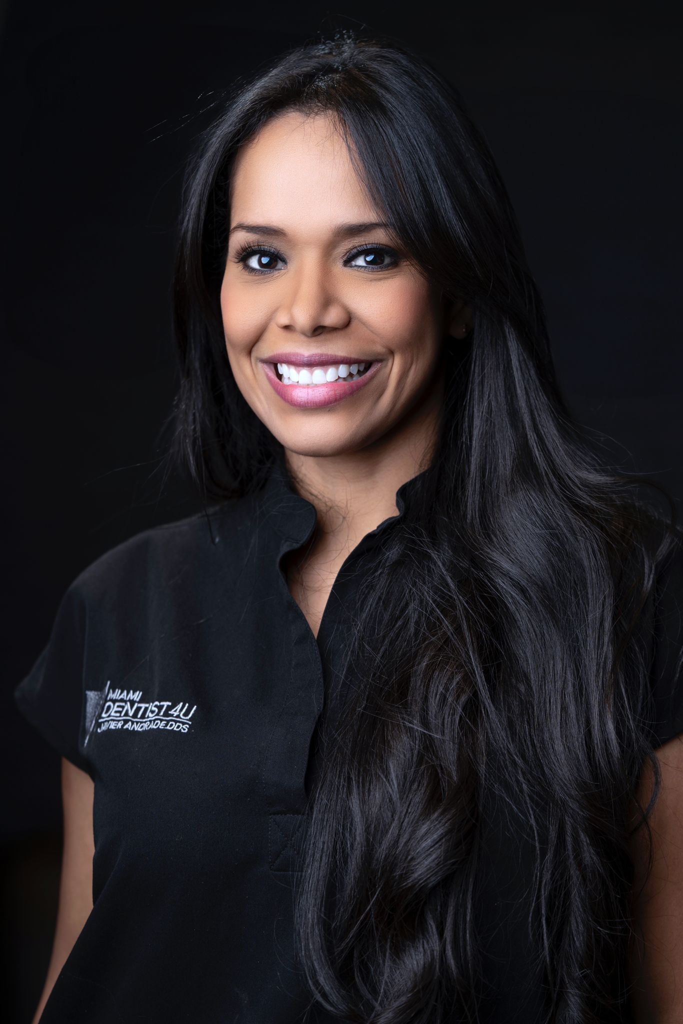 A woman with long black hair is wearing a black shirt and smiling.