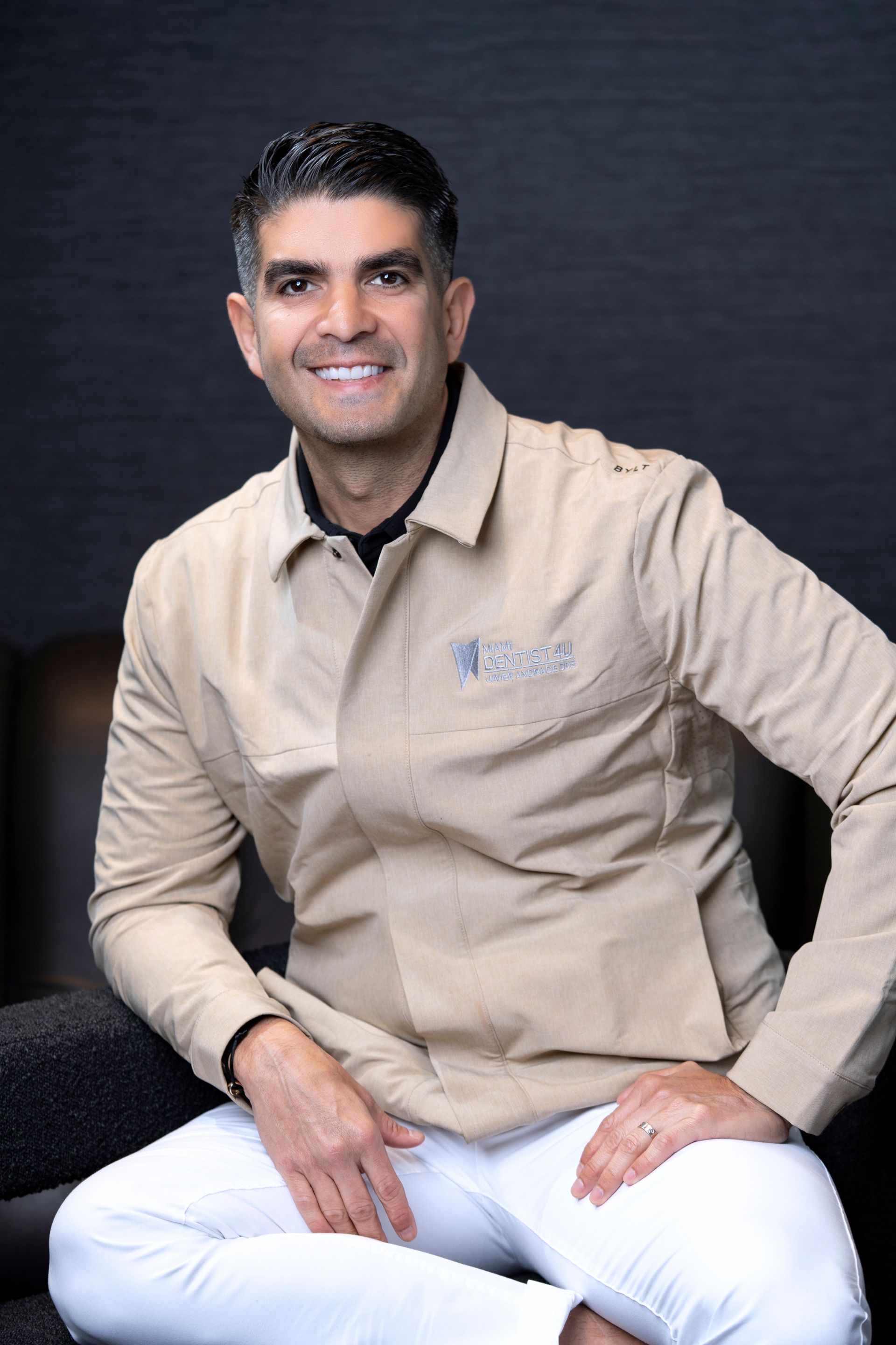 A man is sitting on a chair with his legs crossed and smiling.