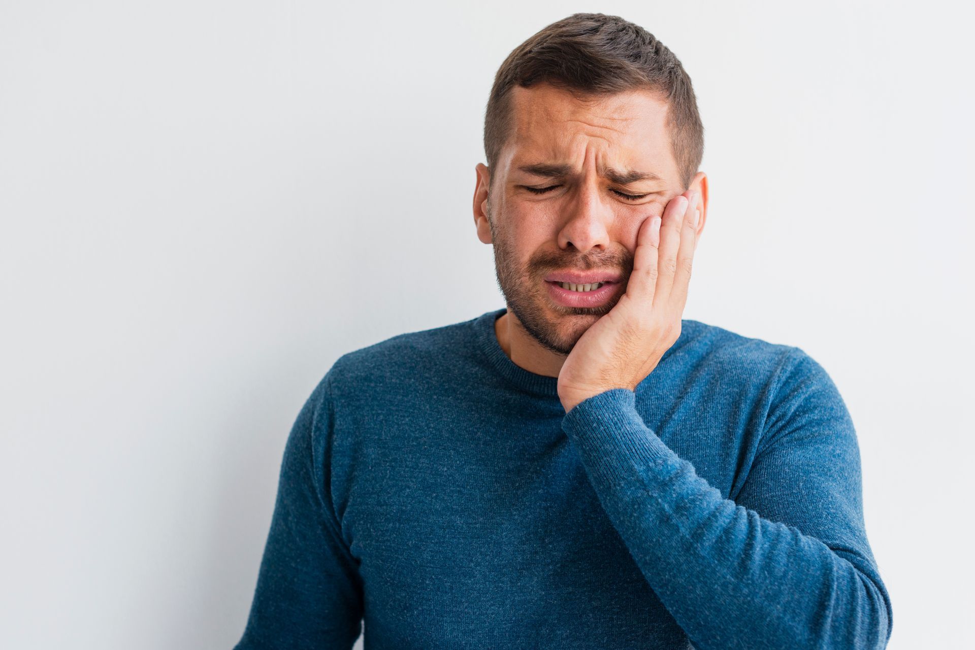 A man in a blue sweater is holding his face in pain.