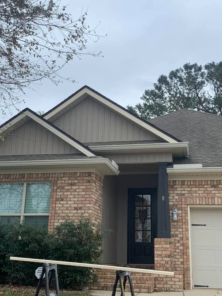 Brick house front entrance with gabled roof, black door, and white garage door under cloudy sky