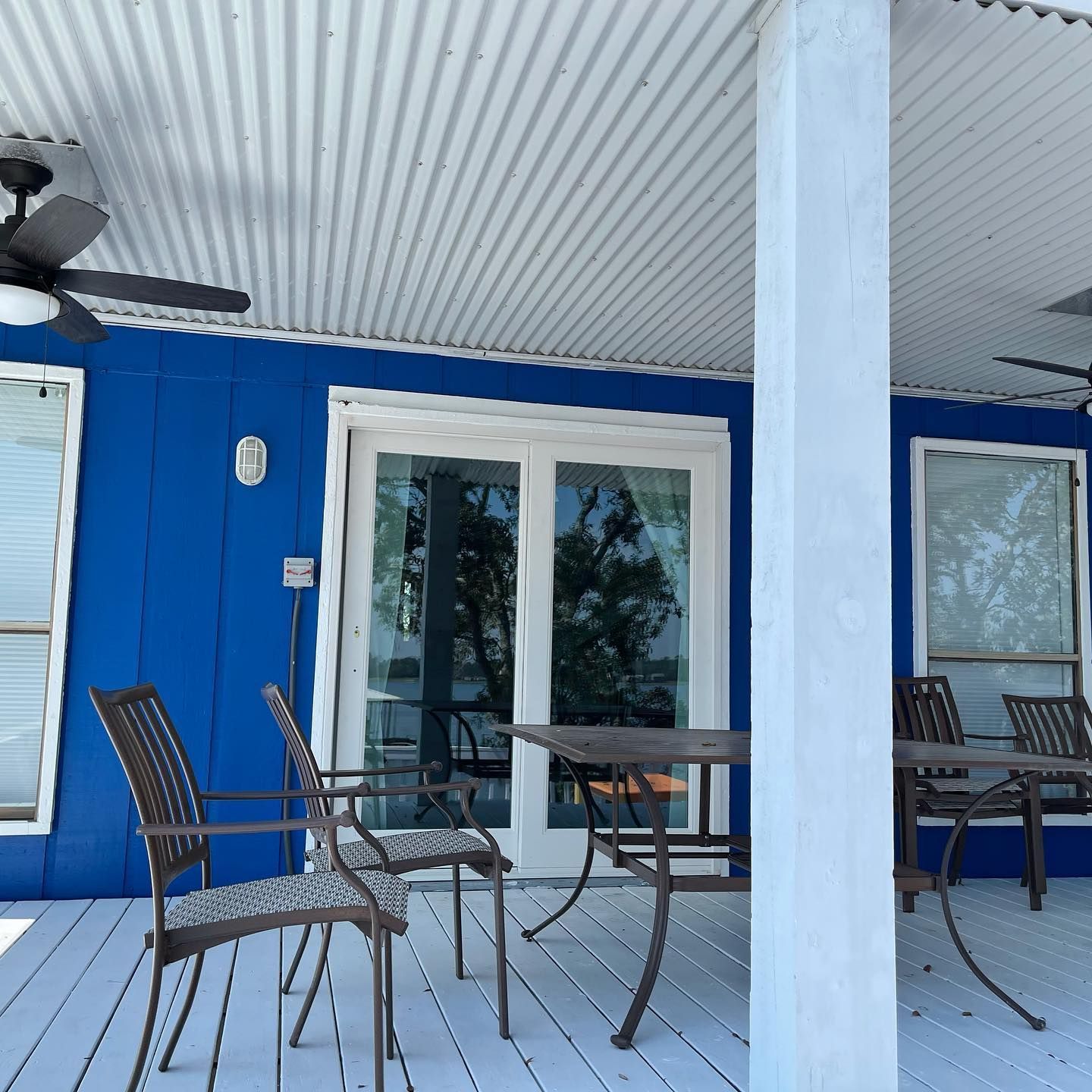 Blue porch with white columns, sliding glass door, and metal patio chairs and table.