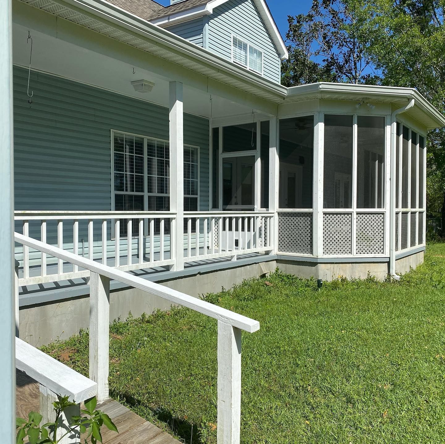 White-railed porch with screened sunroom on a light blue house, beside a grassy yard and steps.