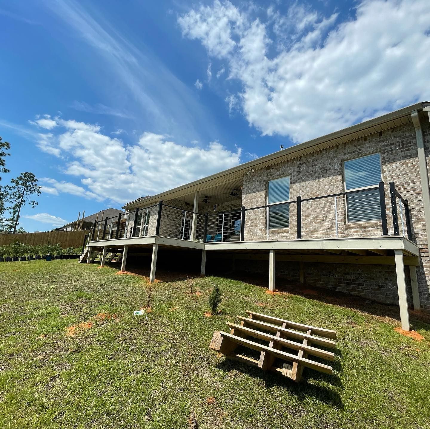 Stone house on stilts with a covered porch on a grassy hillside under a partly cloudy blue sky.