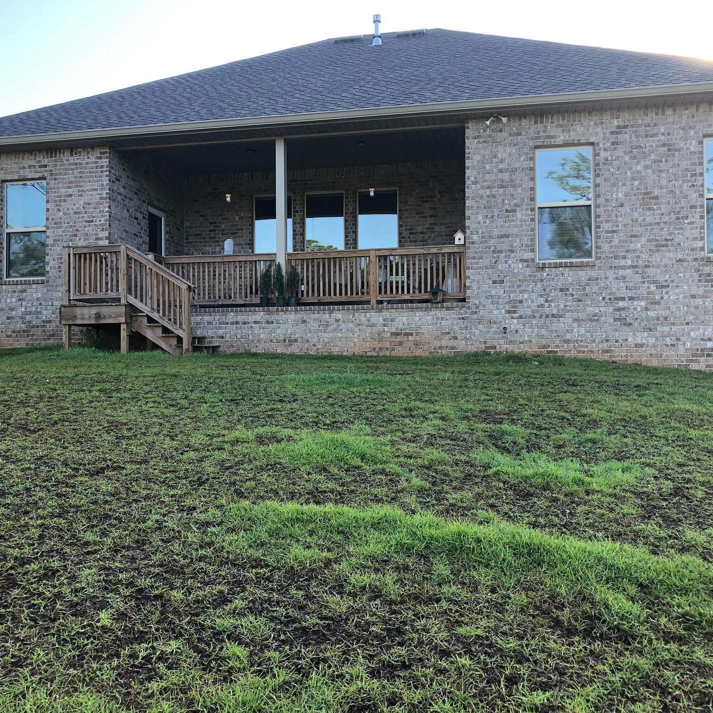 Stone house with a covered porch, wooden steps, and a grassy yard under a blue sky