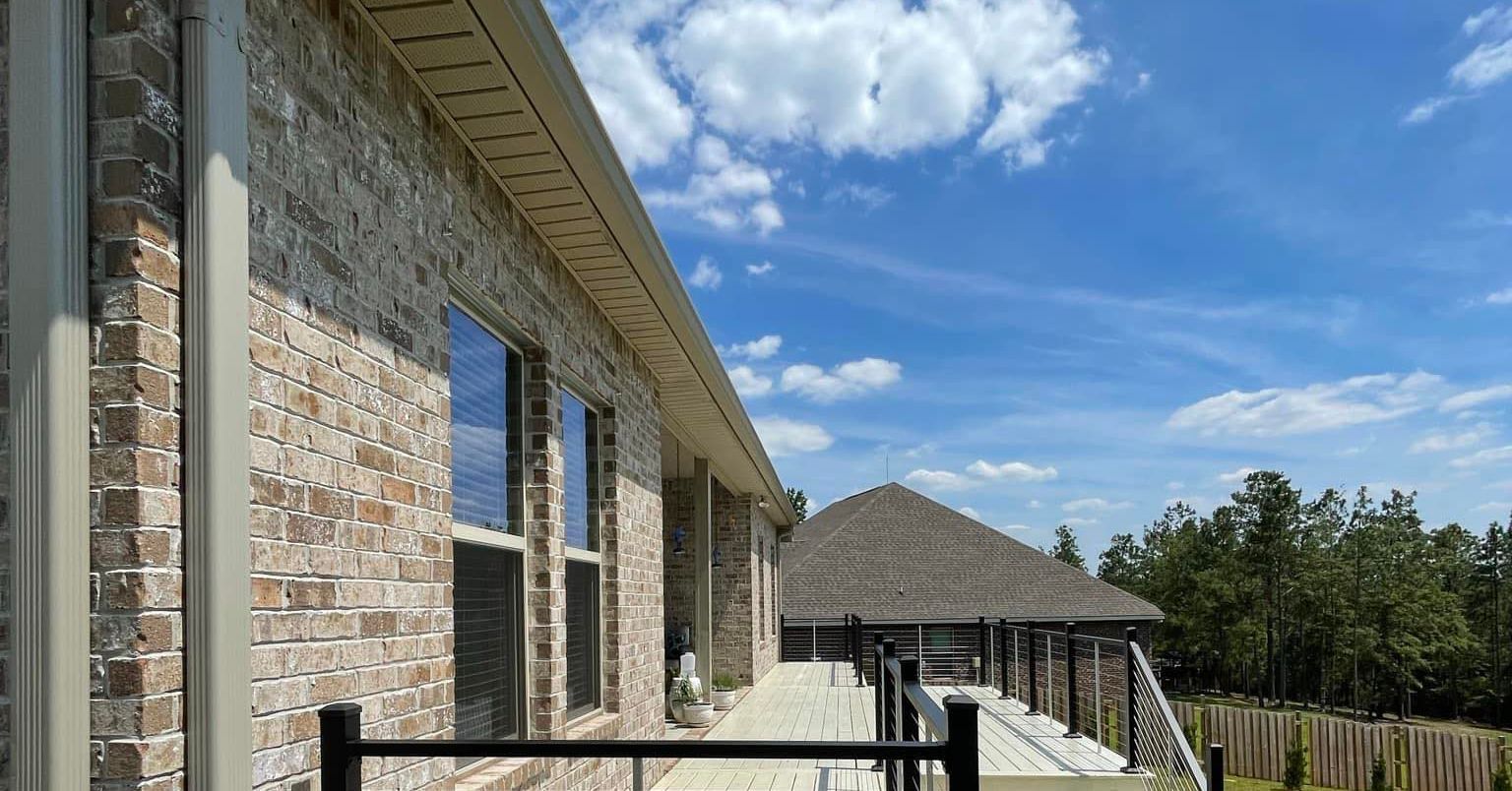 Brick house exterior with large windows, a fenced patio, and a blue sky with clouds