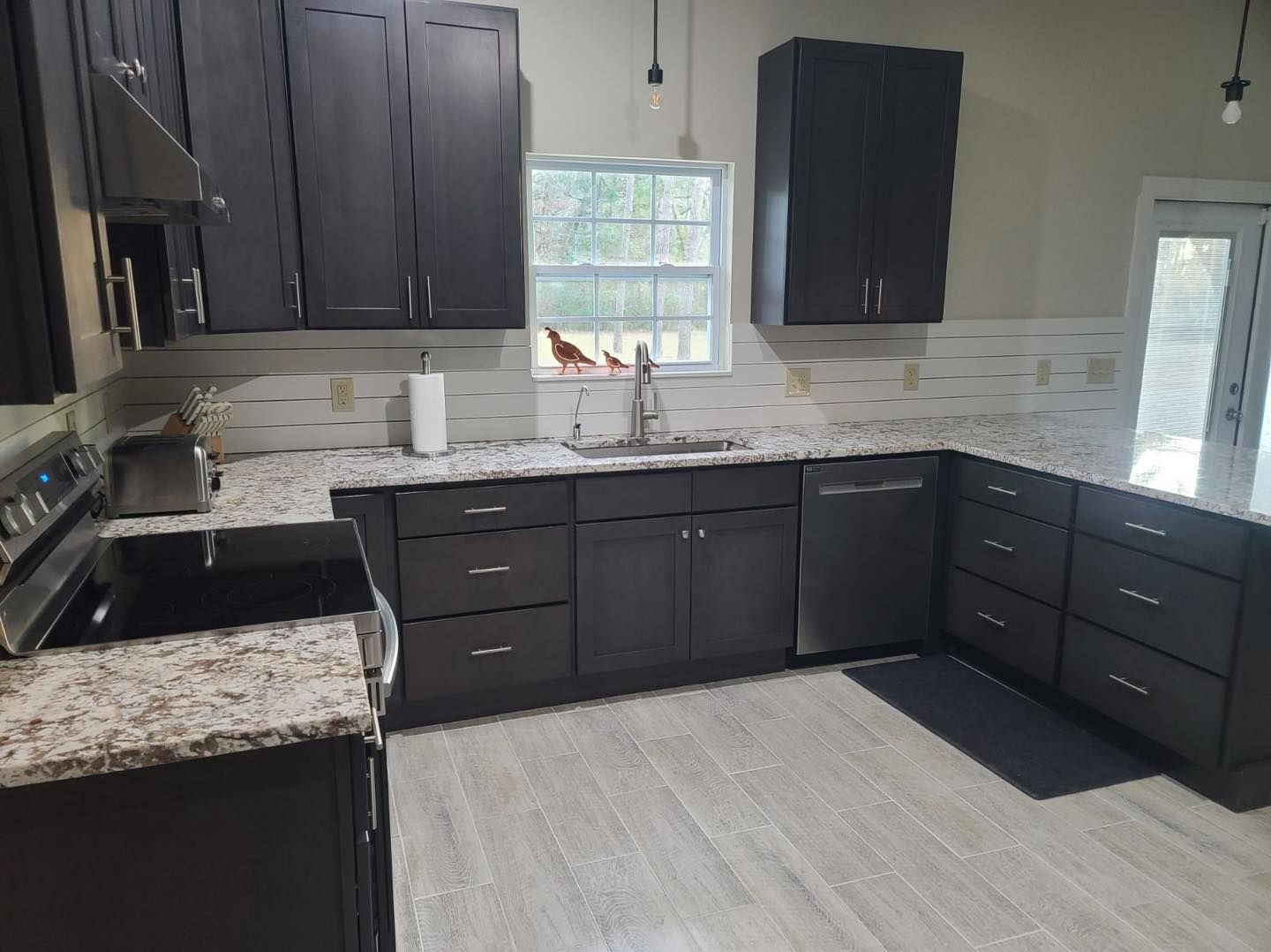 Modern kitchen with dark gray cabinets, granite countertops, stainless steel appliances, and light gray flooring.