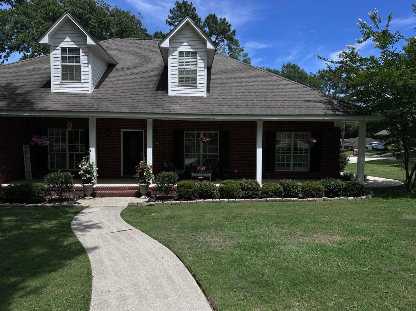 Suburban house with white dormer windows, dark roof, and a curved walkway through the front lawn