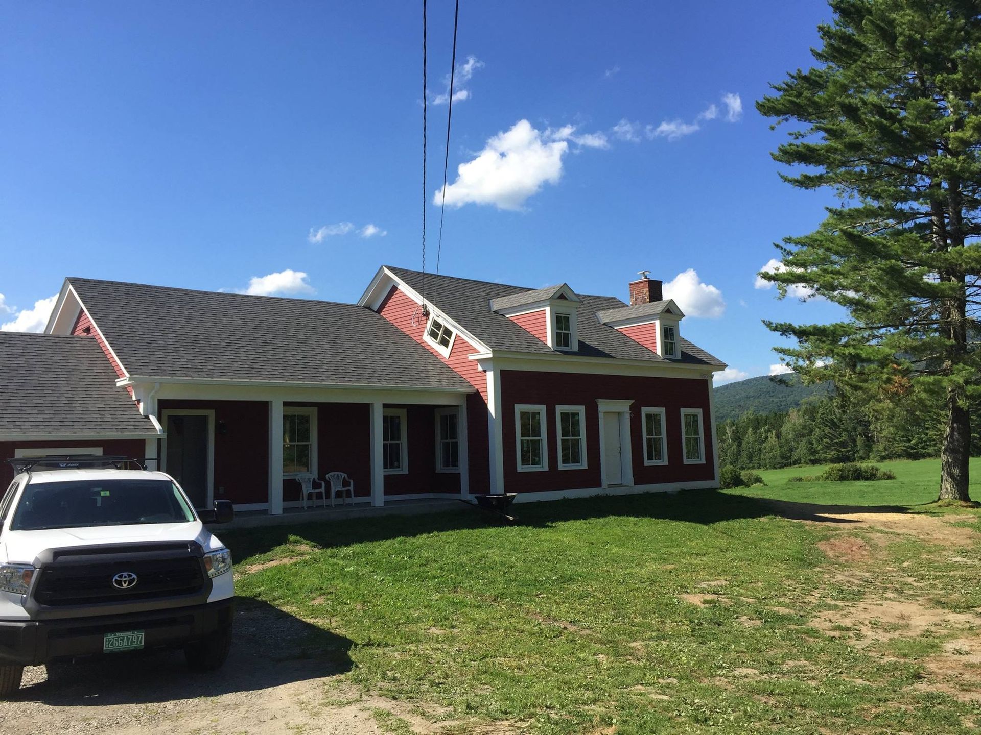 Red house with white trim and parked SUV on a grassy yard under a blue sky