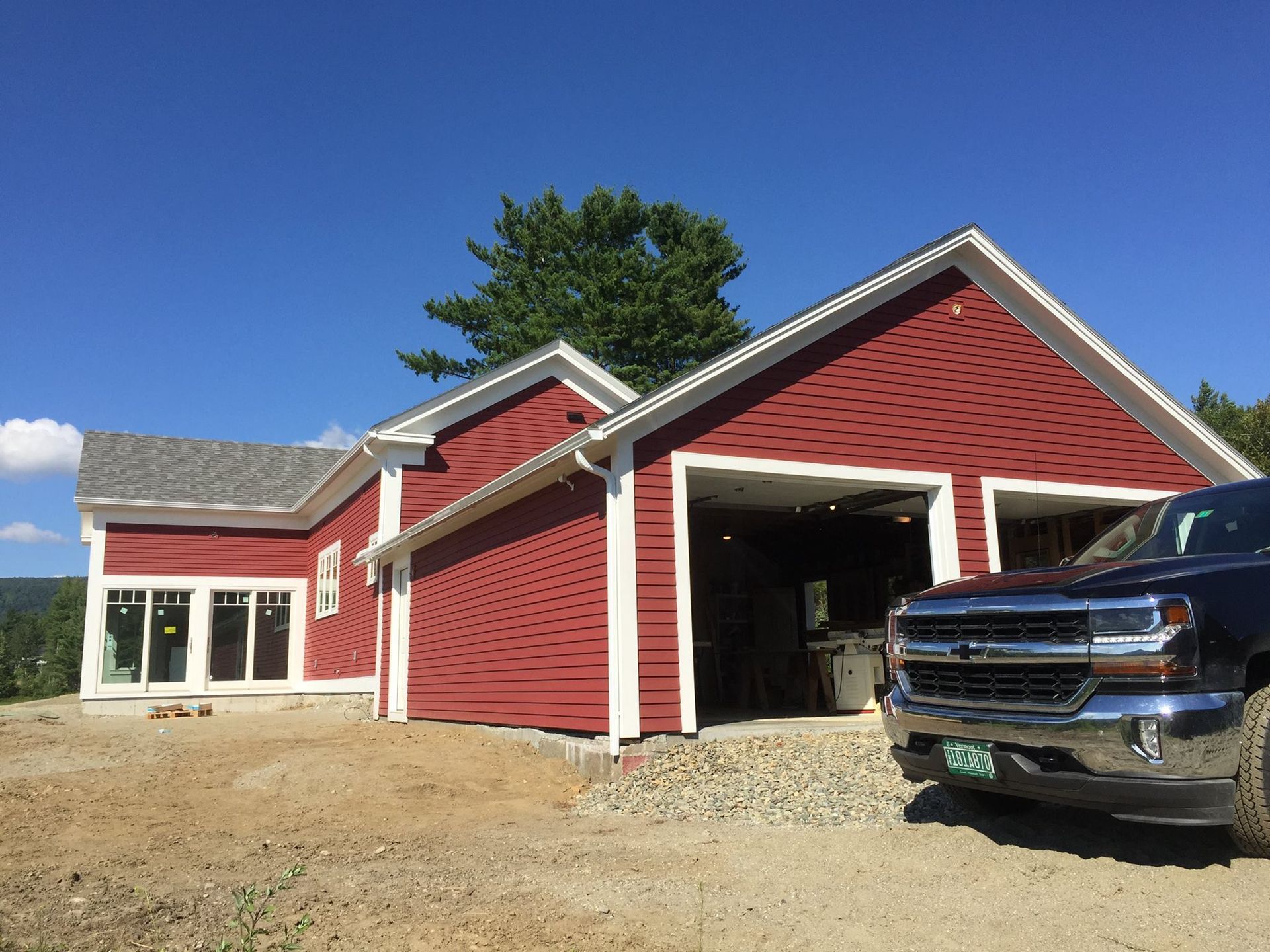 Red house with open garage and black truck parked in front on a gravel driveway.