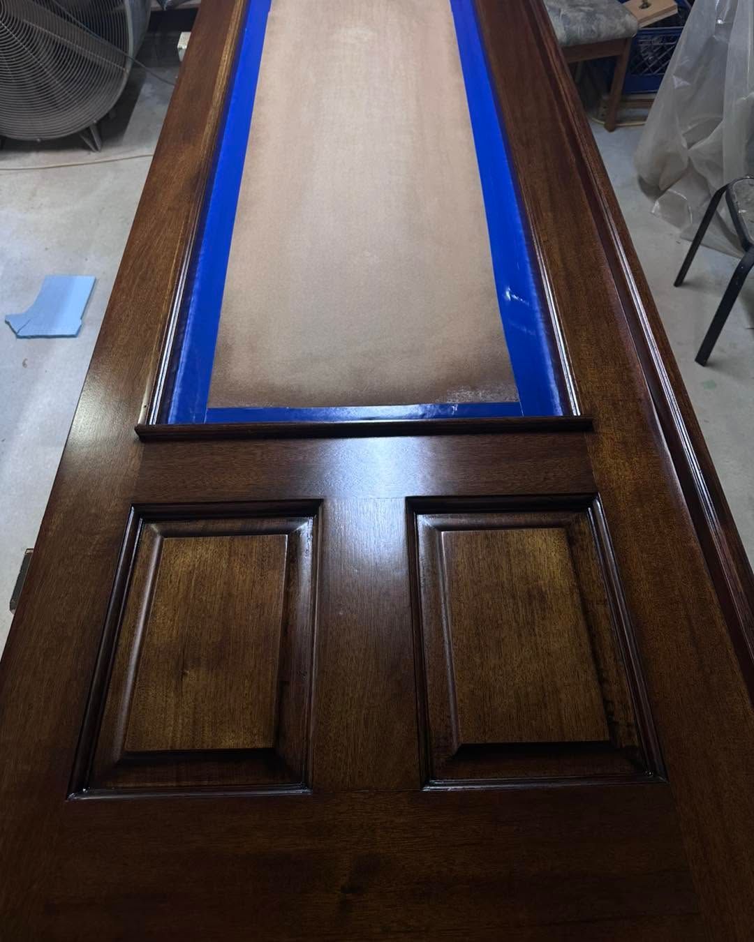 Wooden door with dark stain and blue painter’s tape around the upper panel opening