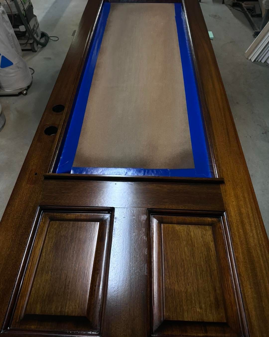 Wooden door with a rectangular cutout covered by blue tape and brown paper masking material