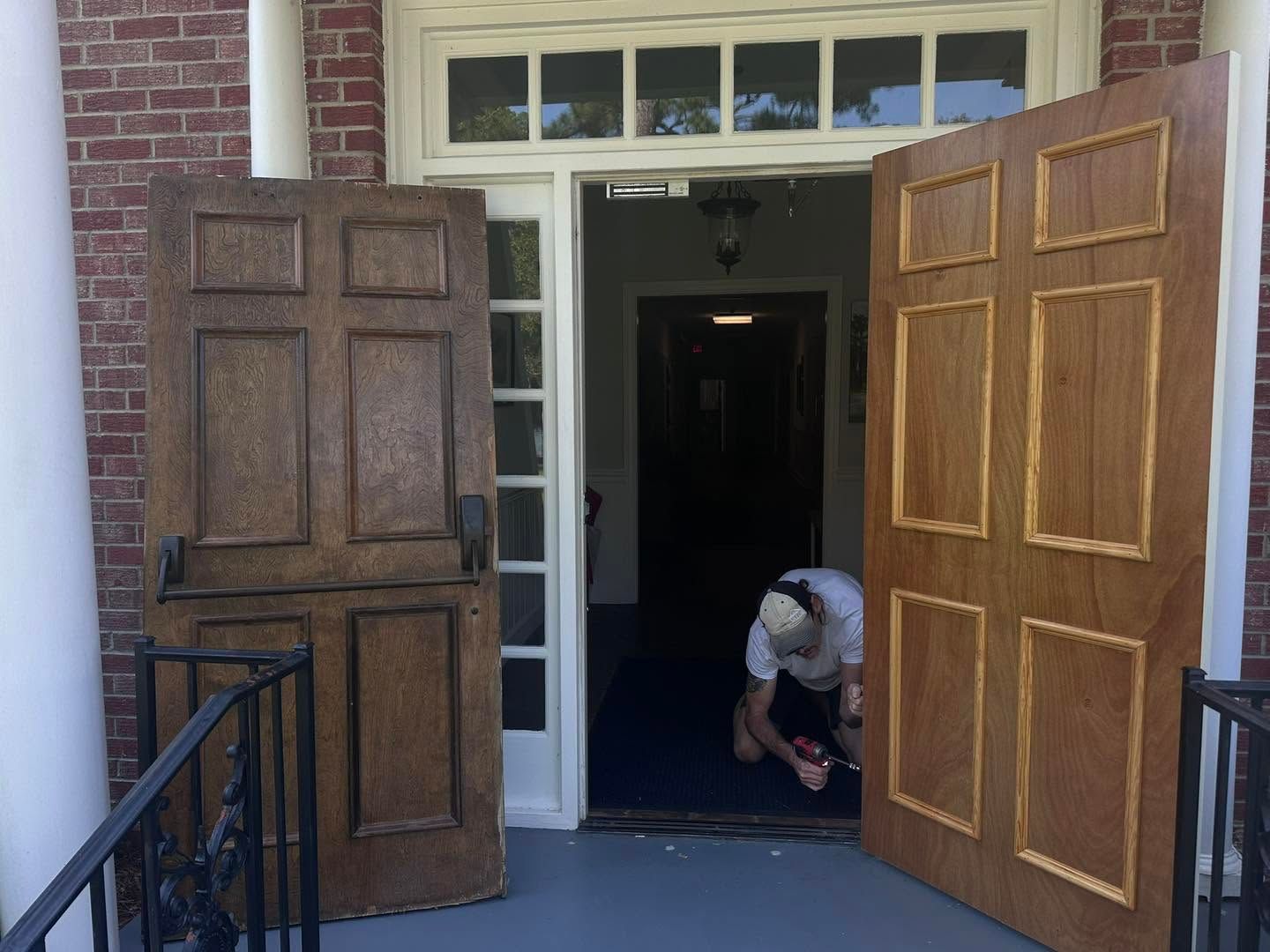 Open double wooden doors at a building entrance, with a person crouching inside near the doorway.