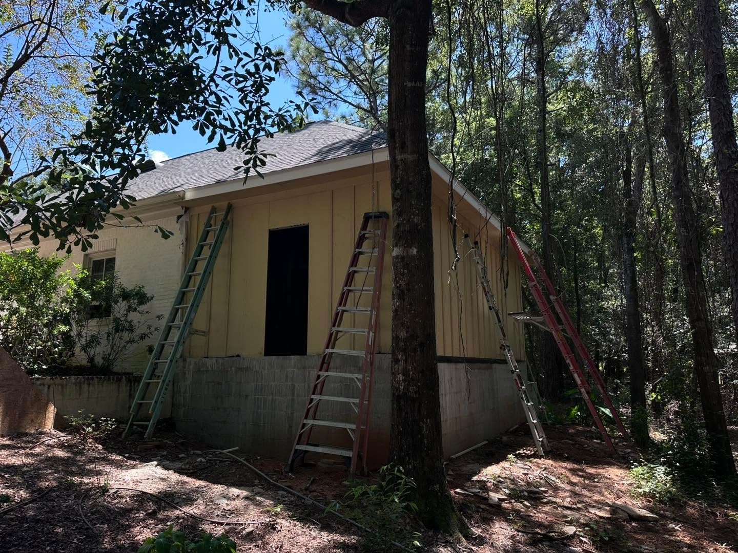 Small beige house under construction in wooded area, with ladders leaning against the walls.