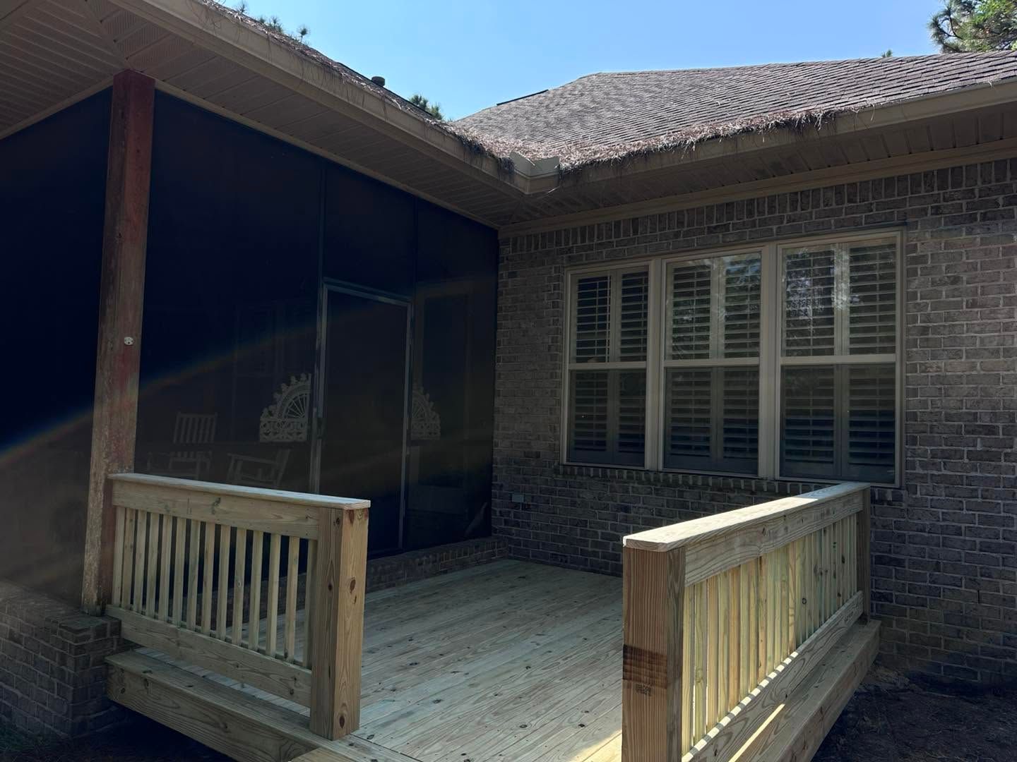 Covered wooden porch attached to a brick house with railings and windows.