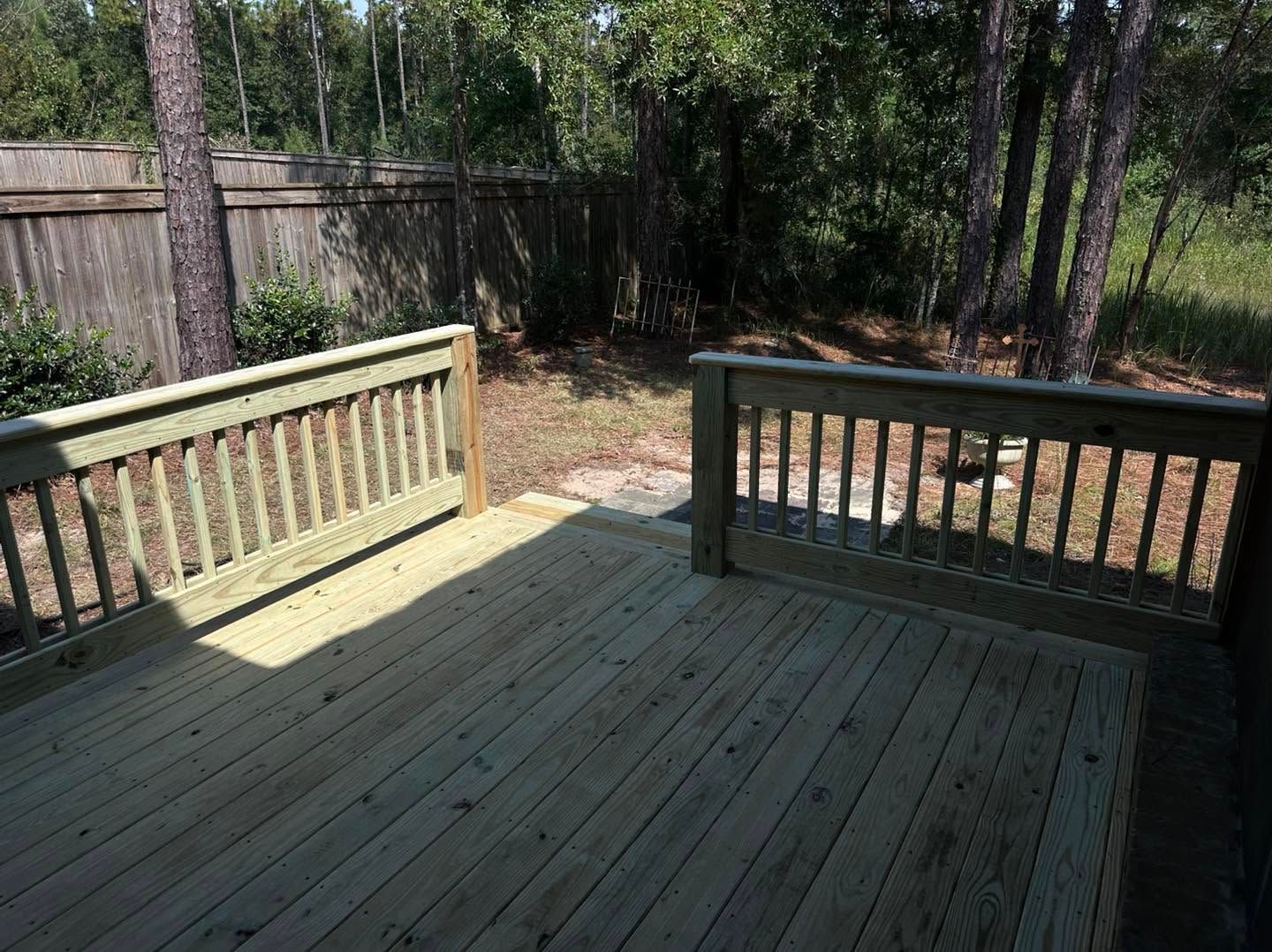 Wooden backyard deck with railings, surrounded by trees and a fenced yard.