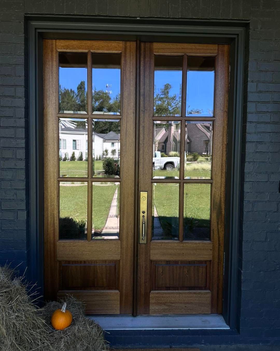Wooden double front doors with glass panes reflecting a sunny street and white houses beyond.