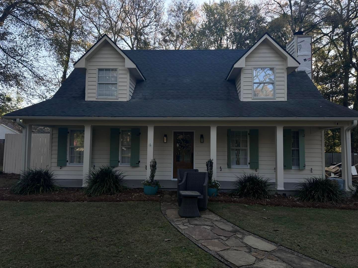 Two-story white house with green shutters, dark roof, and a front porch at dusk