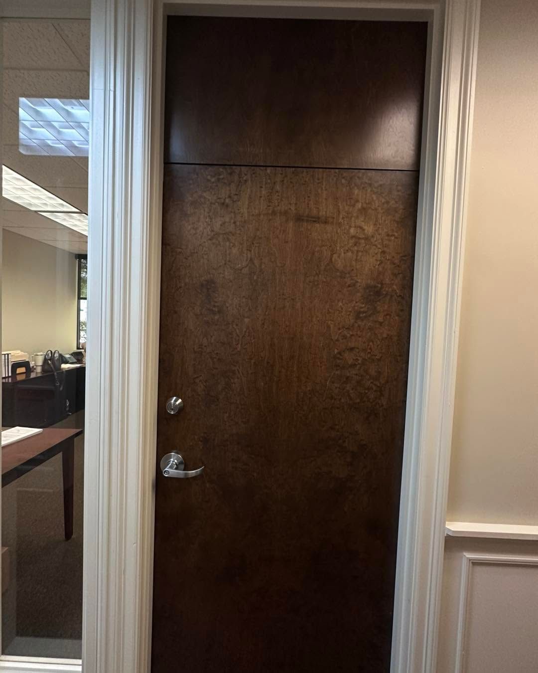 Brown wooden door with silver handle and frame in an office hallway