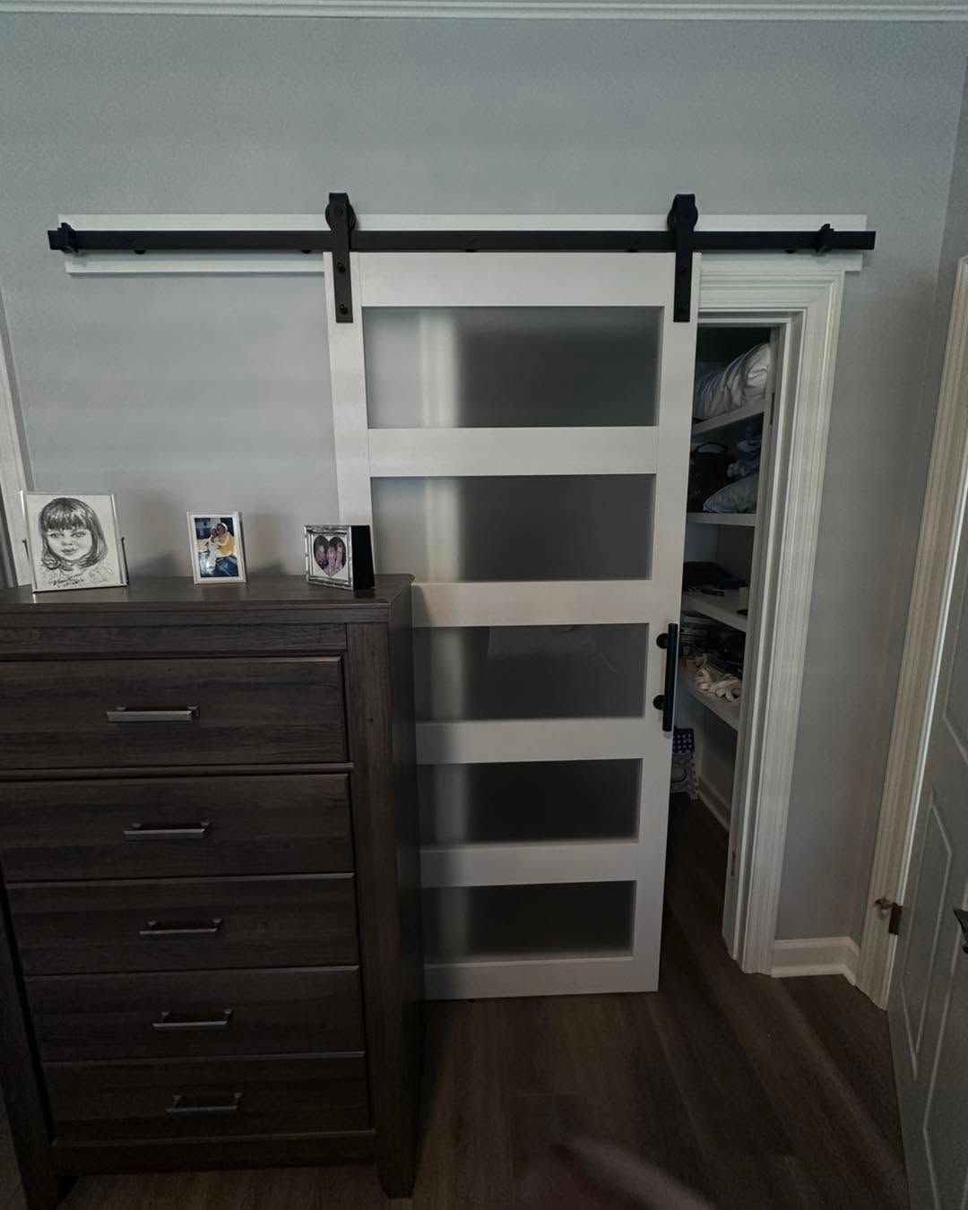 White sliding barn door with frosted panels partly open to a closet in a bedroom.