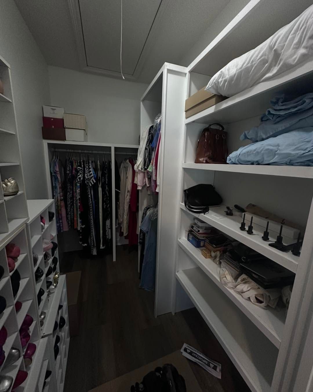 Walk-in closet with shelves, hanging clothes, folded linens, and shoes on the right side.