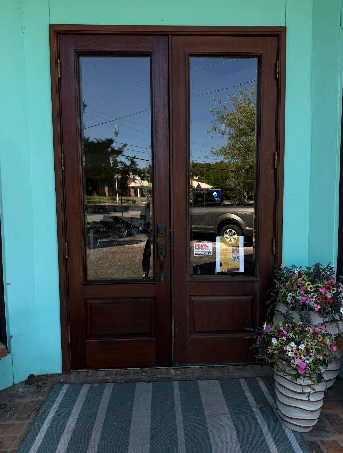 Wooden double doors with glass panels, flanked by turquoise walls, beside a potted flower arrangement.