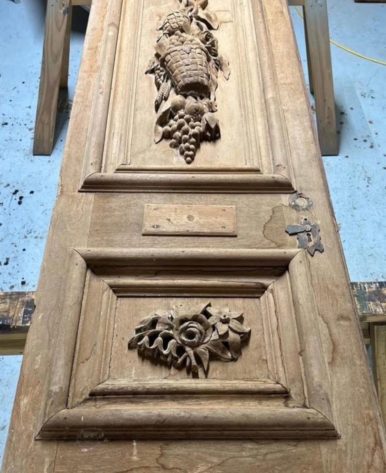 Close-up of a carved wooden door panel with floral relief details and a metal latch on the right.