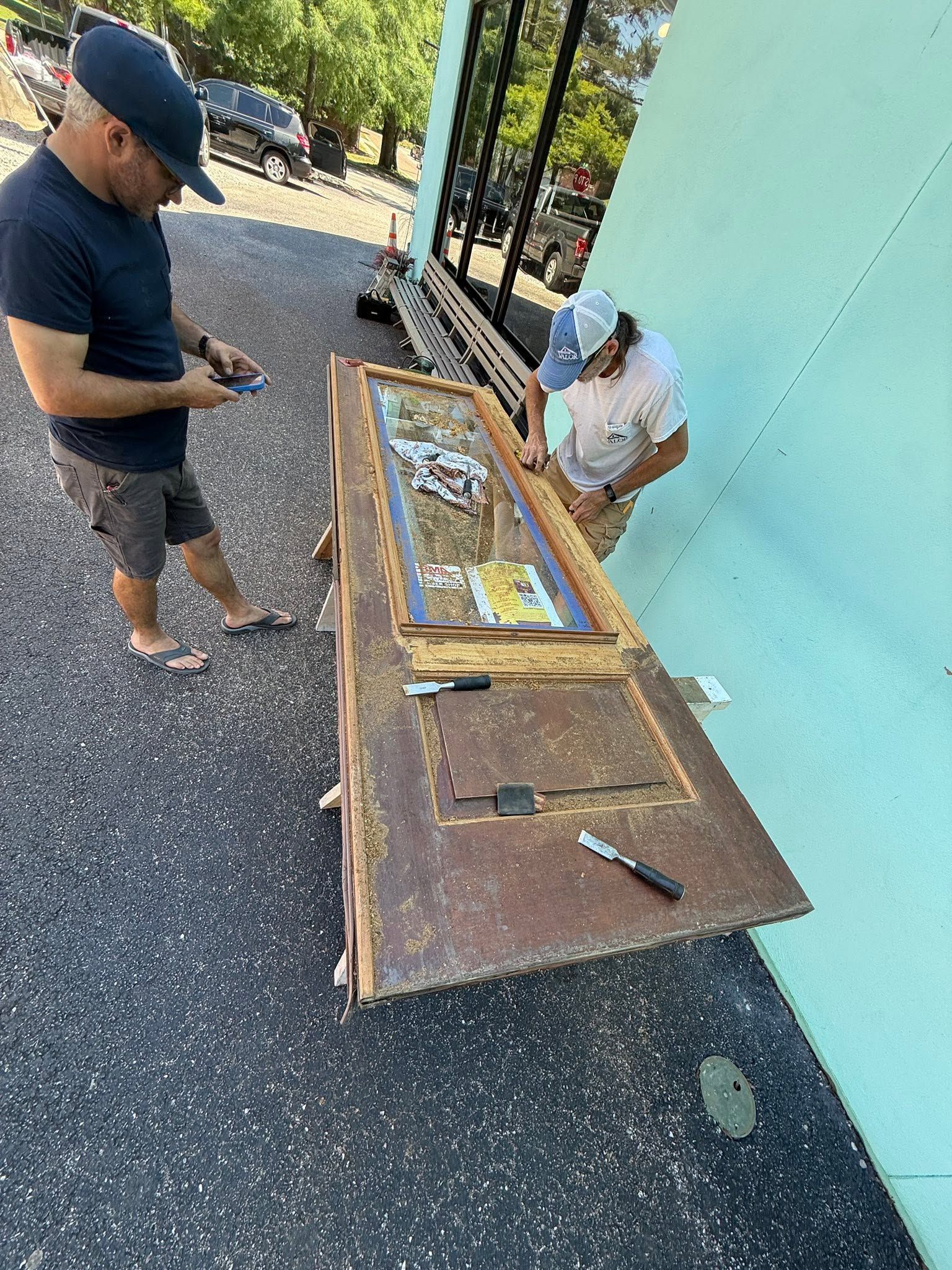 Person using a phone beside an open wooden cabinet outdoors near a turquoise wall.