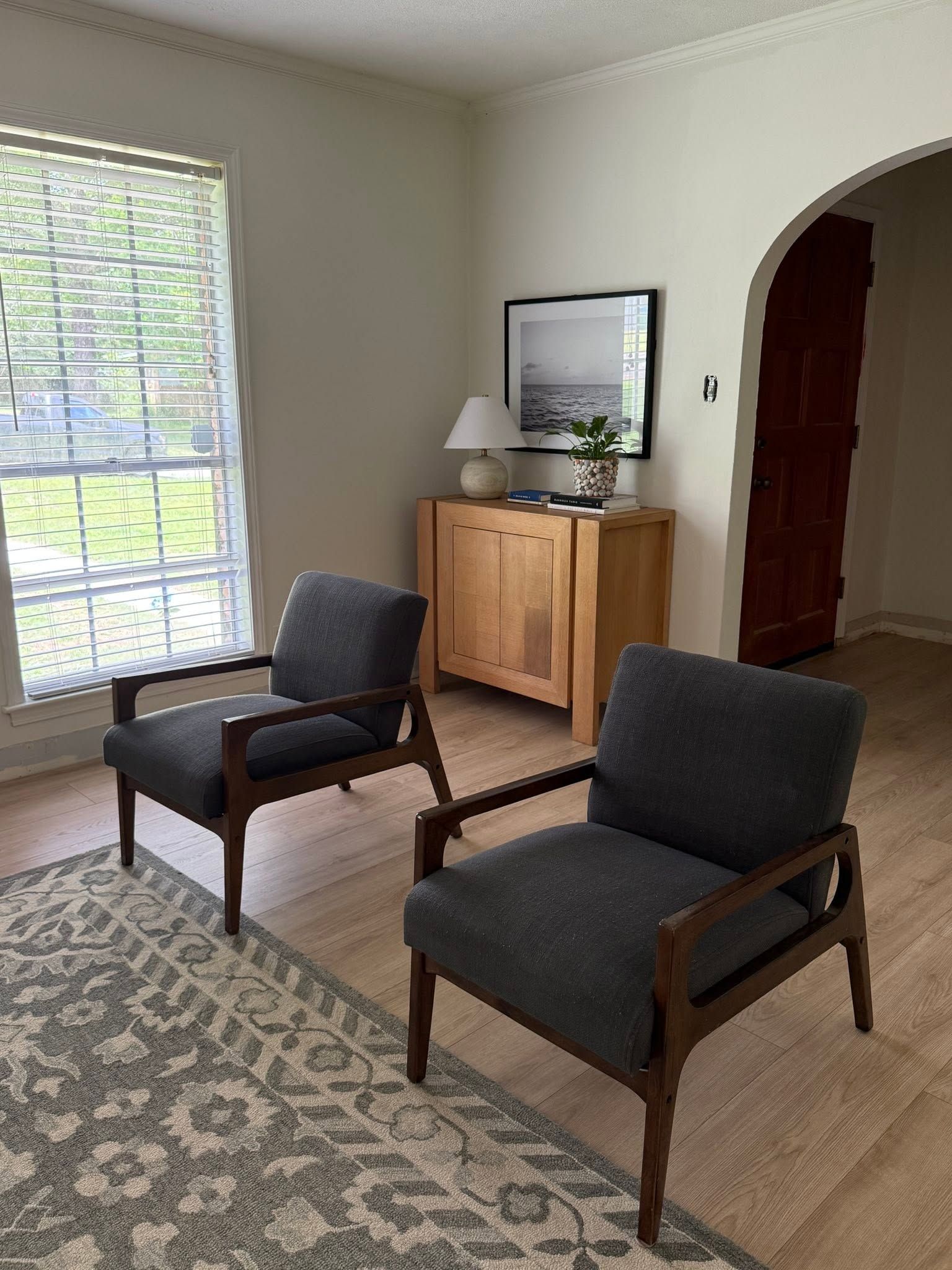 Living room with two dark armchairs, patterned rug, wooden cabinet, and a window with blinds