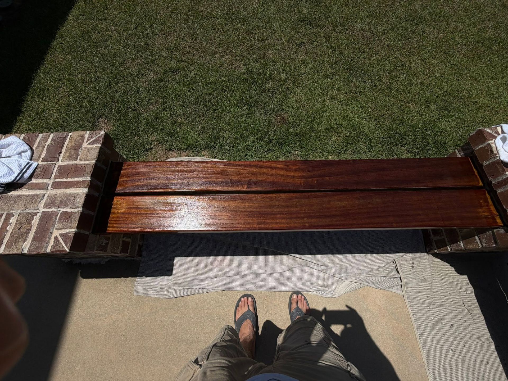 View from a porch toward a wooden bench on grass, with shoes and feet visible at the bottom.