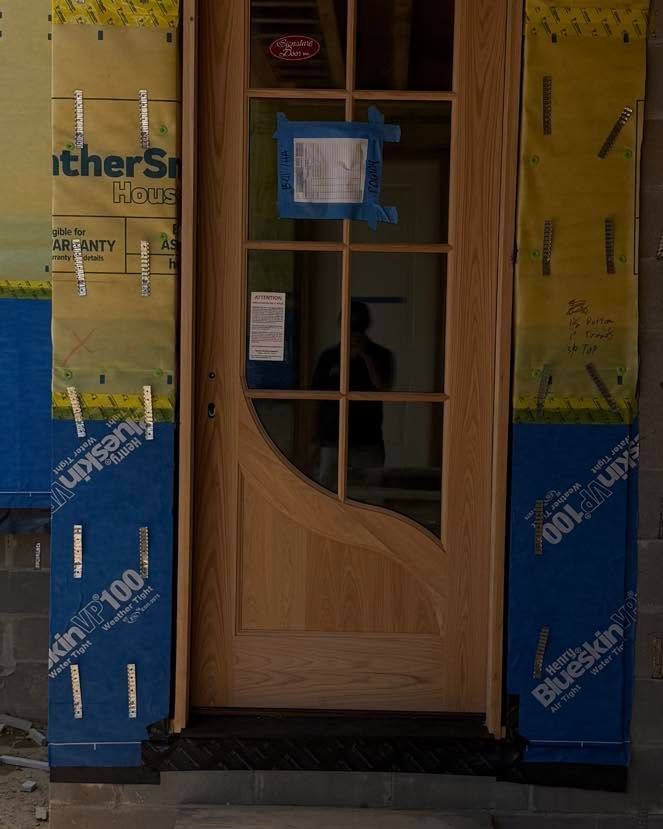 Wooden front door with glass panels, framed by yellow and blue construction wrap.