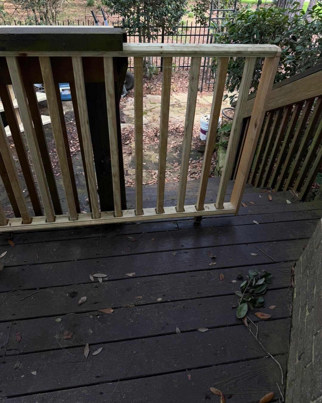 Wooden deck with railings overlooking a yard, scattered leaves, and a small plant by the corner.